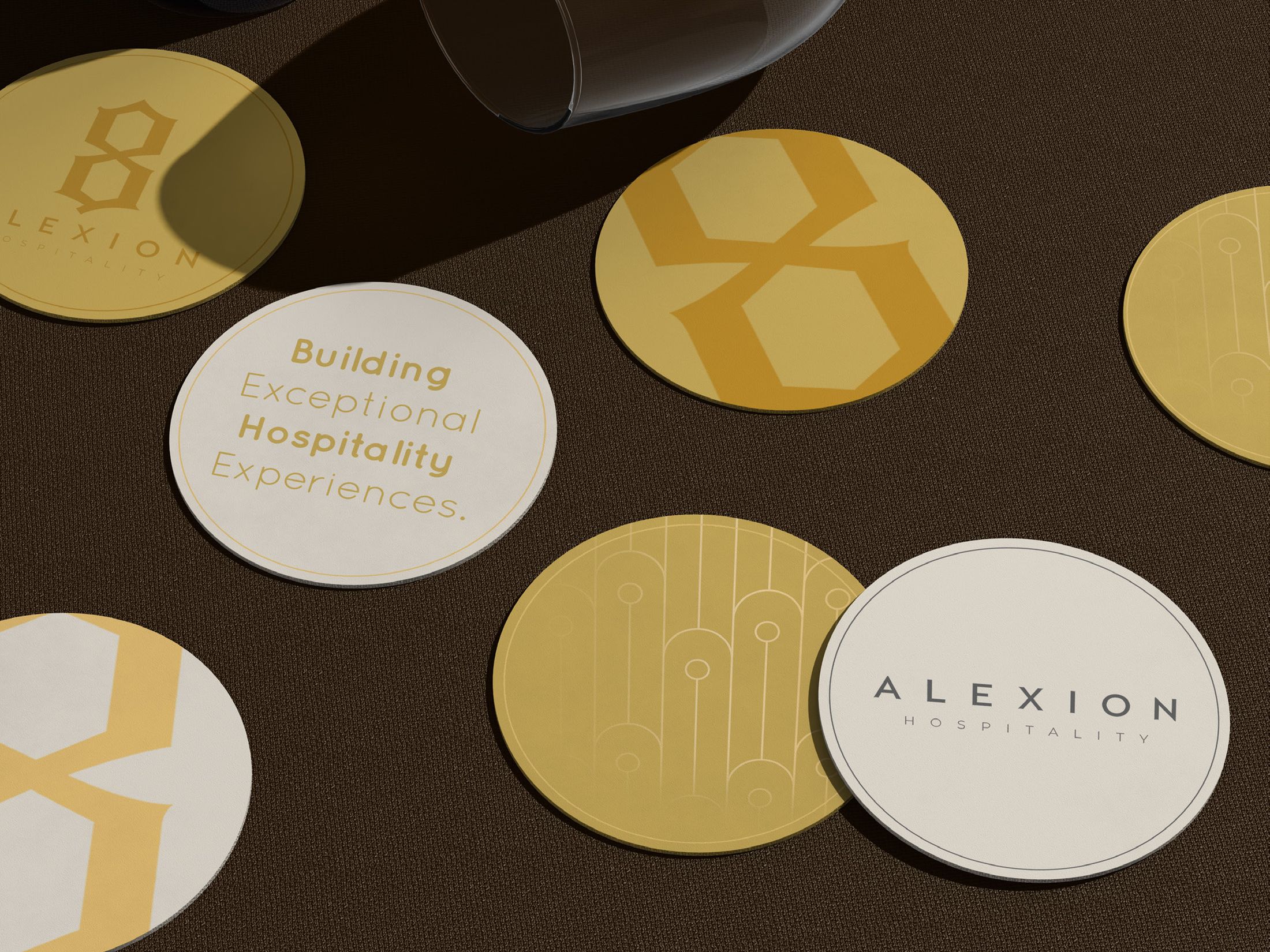 Alexion Hospitality onderzetters in goud en warm beige op een donkere tafel